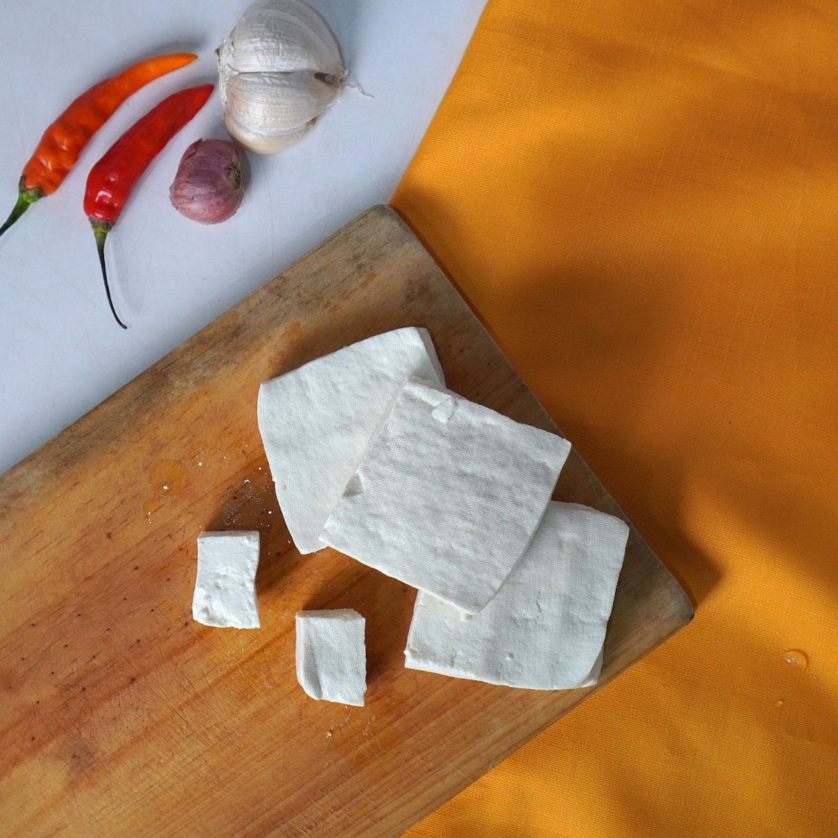 Tranches de tofu ferme sur une planche en bois, avec piments rouges et gousses d'ail